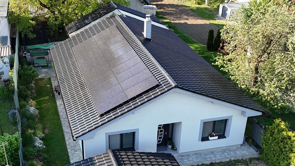 Biely bungalov s čiernymi panelmi na tmavej streche