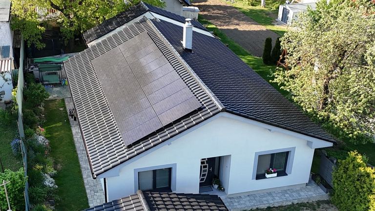 Biely bungalov s čiernymi panelmi na tmavej streche